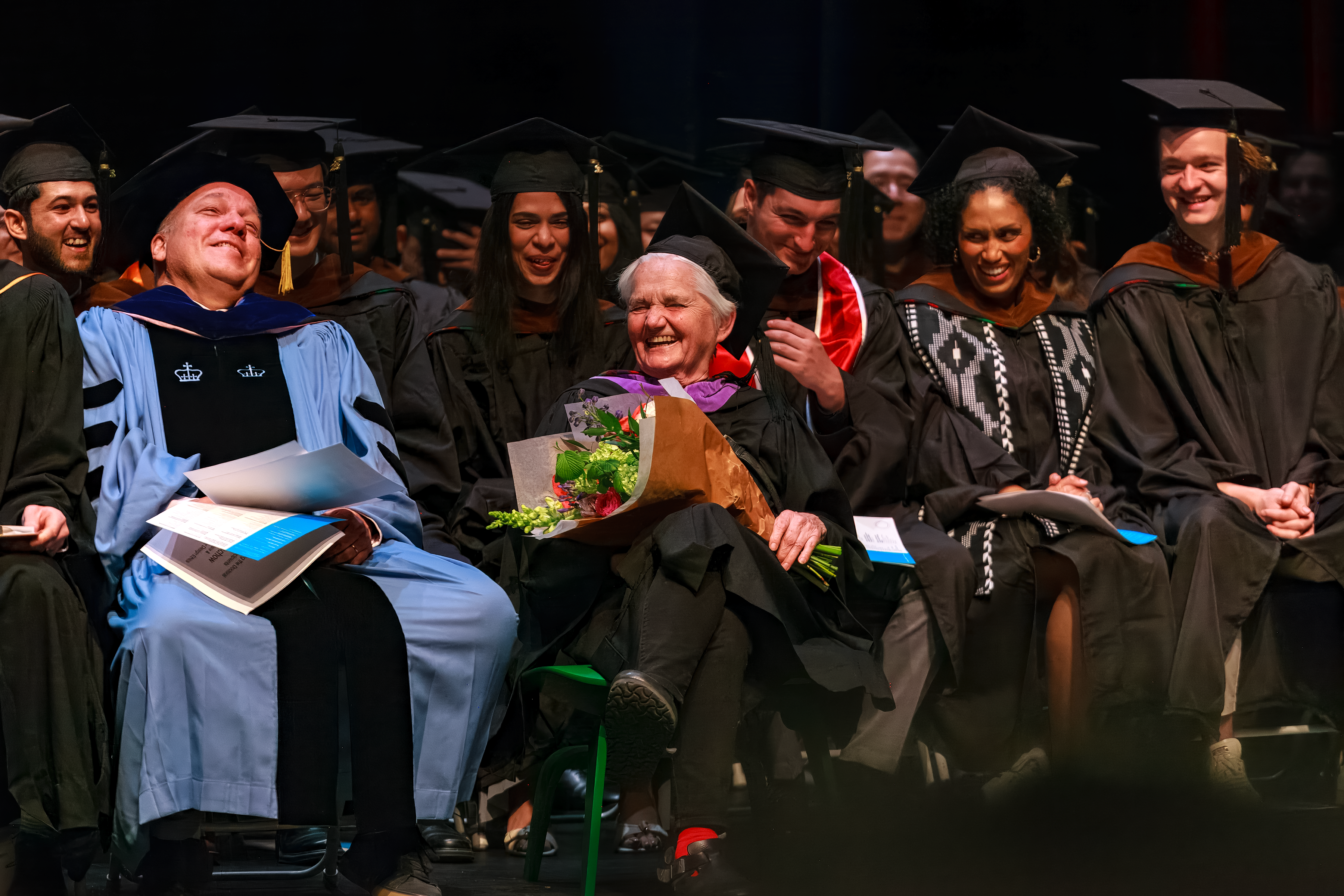 group sitting onstage in graduation regalia