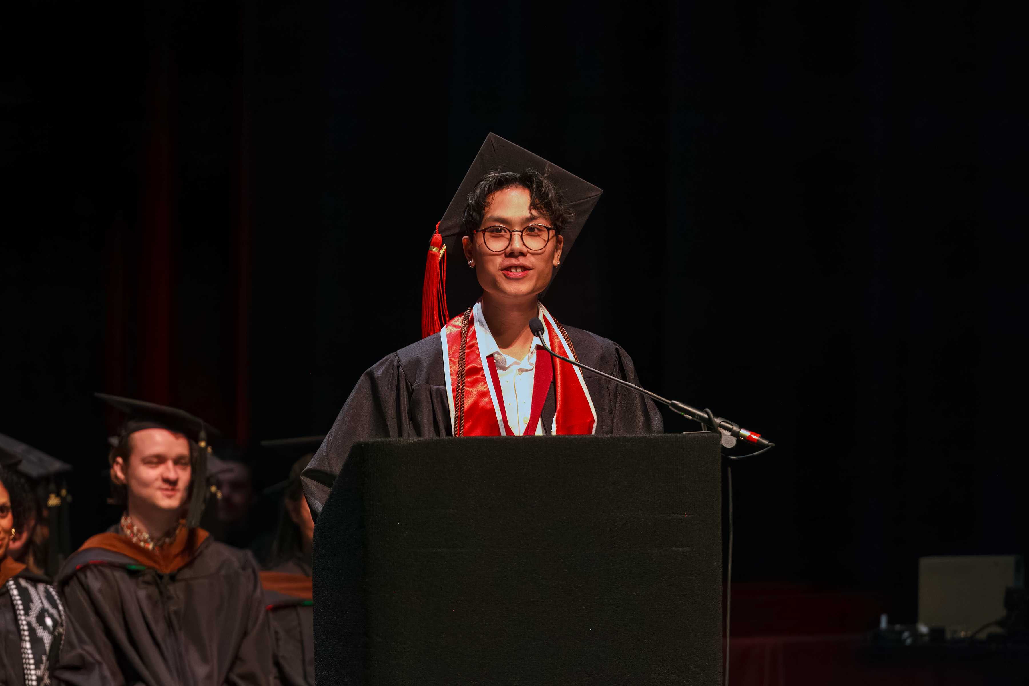 student onstage at podium in graduation regalia