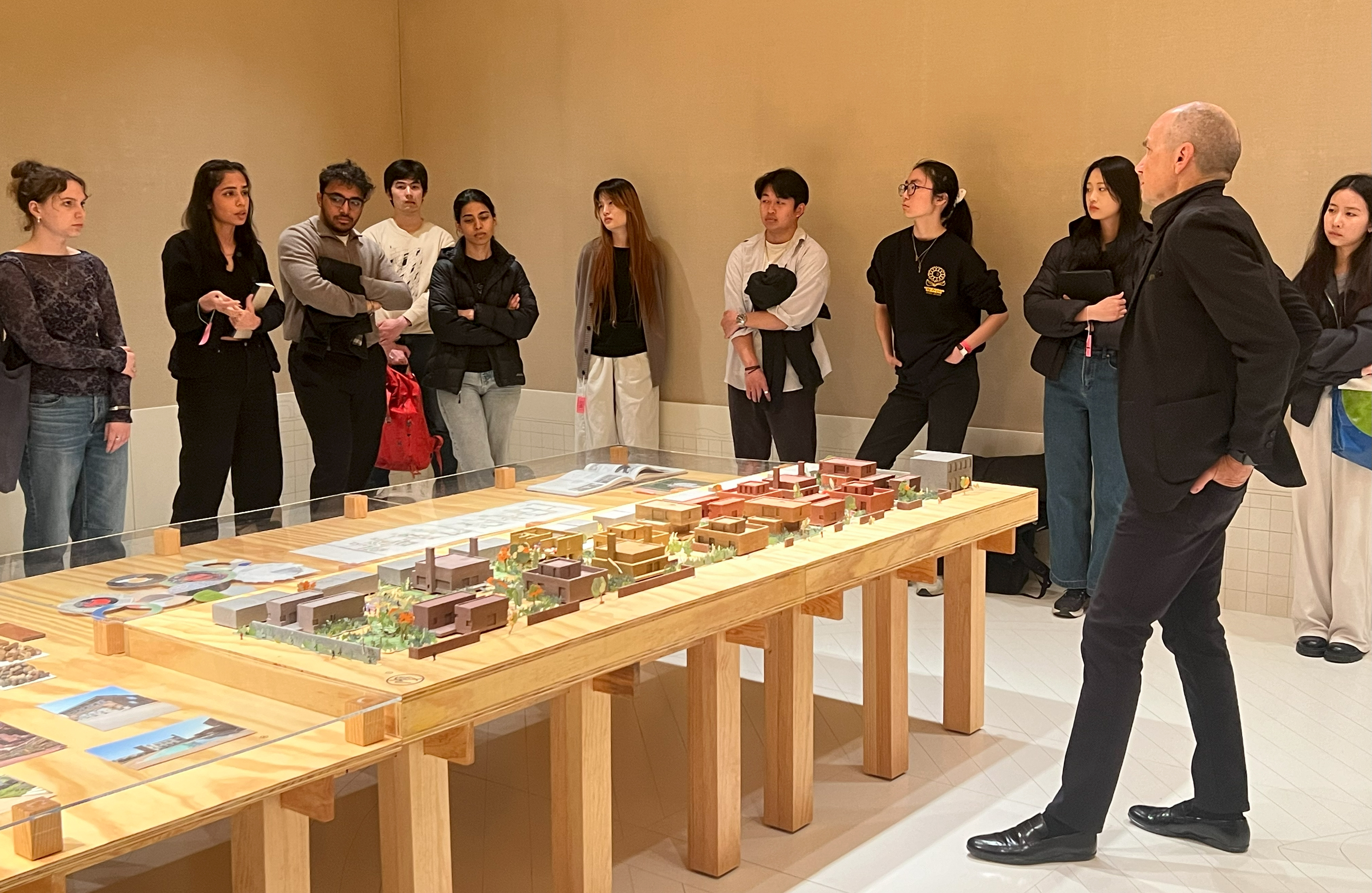 a group of students stands in a group around an exhibition on a large table