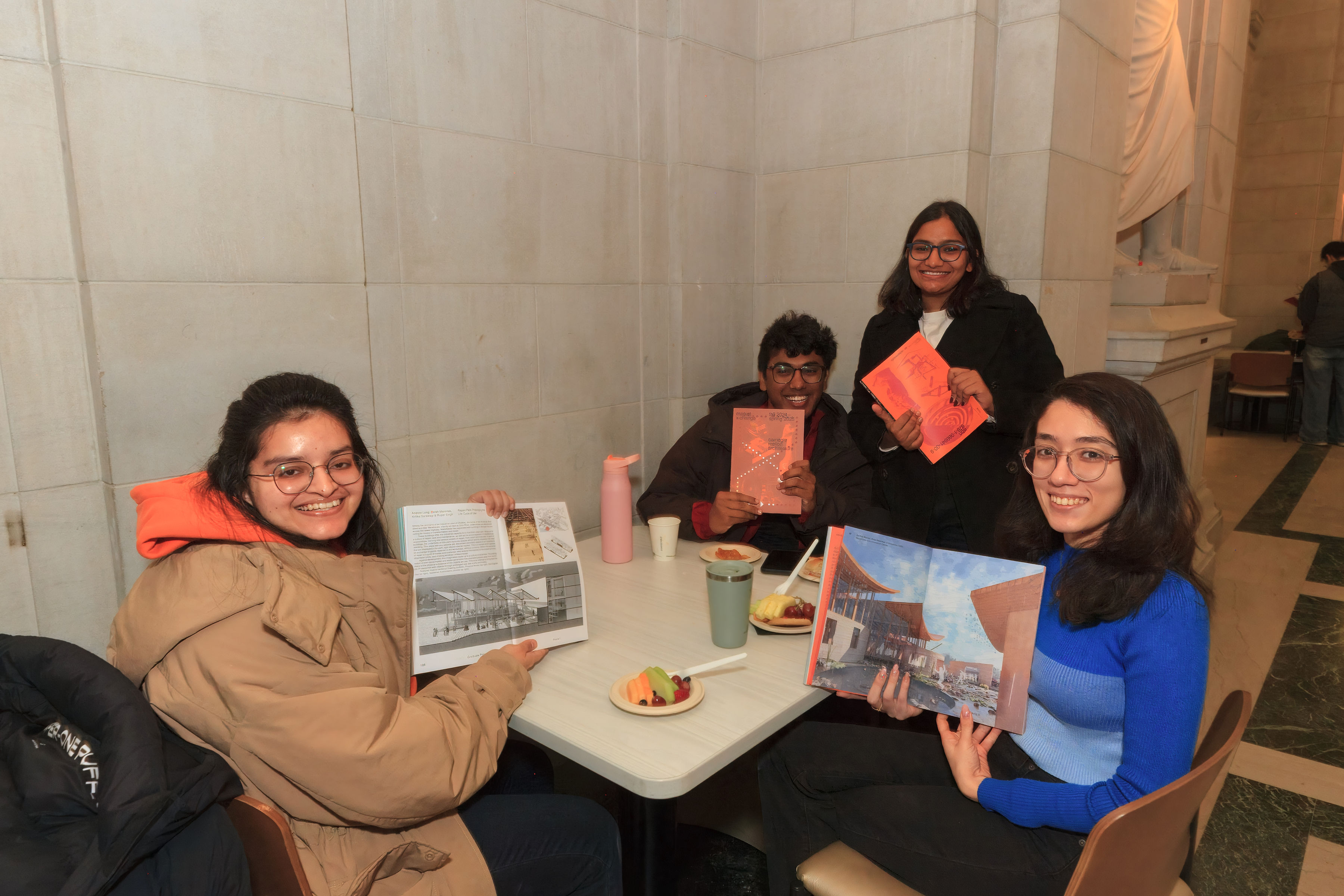 students sit around a table with books and plates of fruit