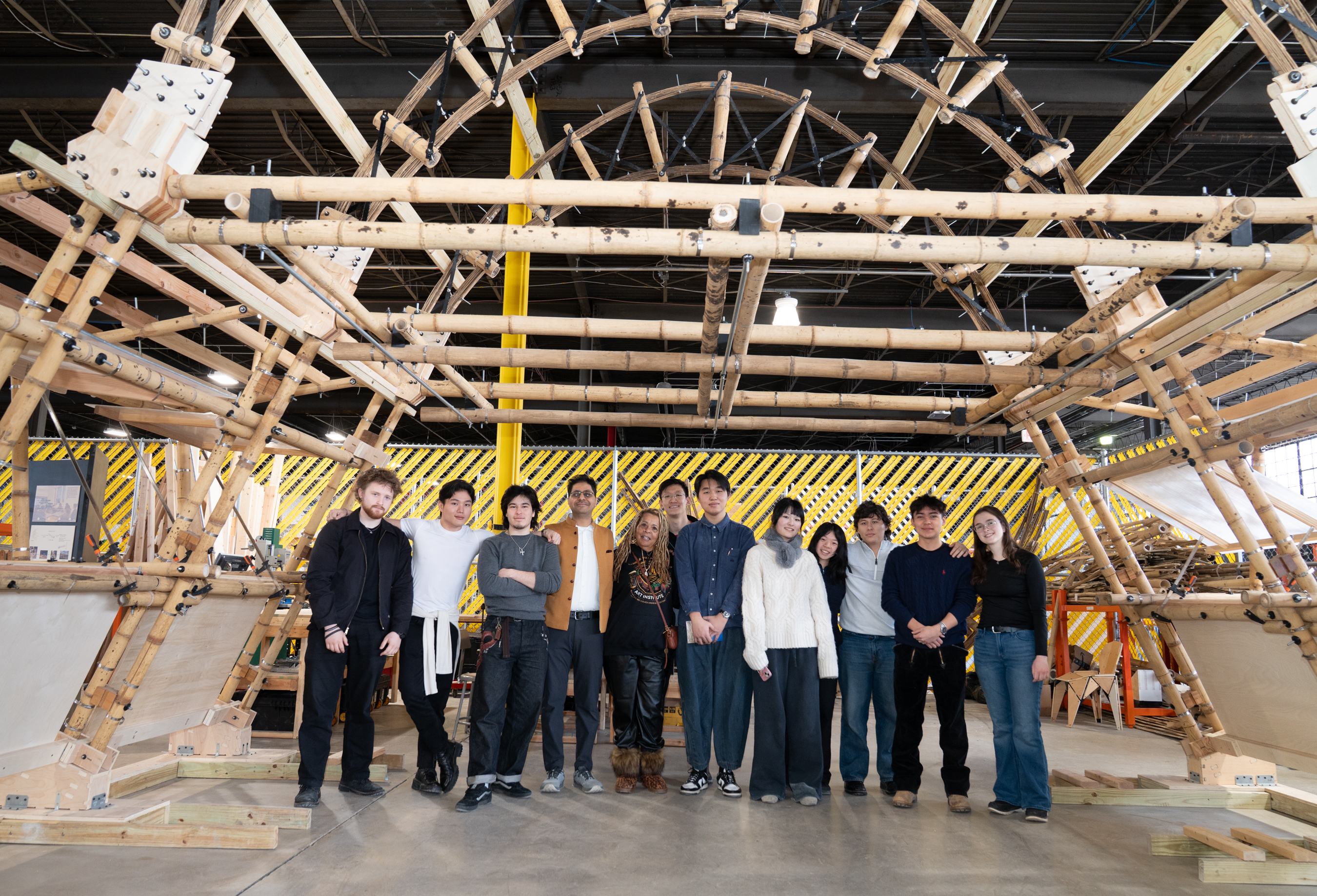 a project team poses underneath the large bamboo structure they built as part of their project.