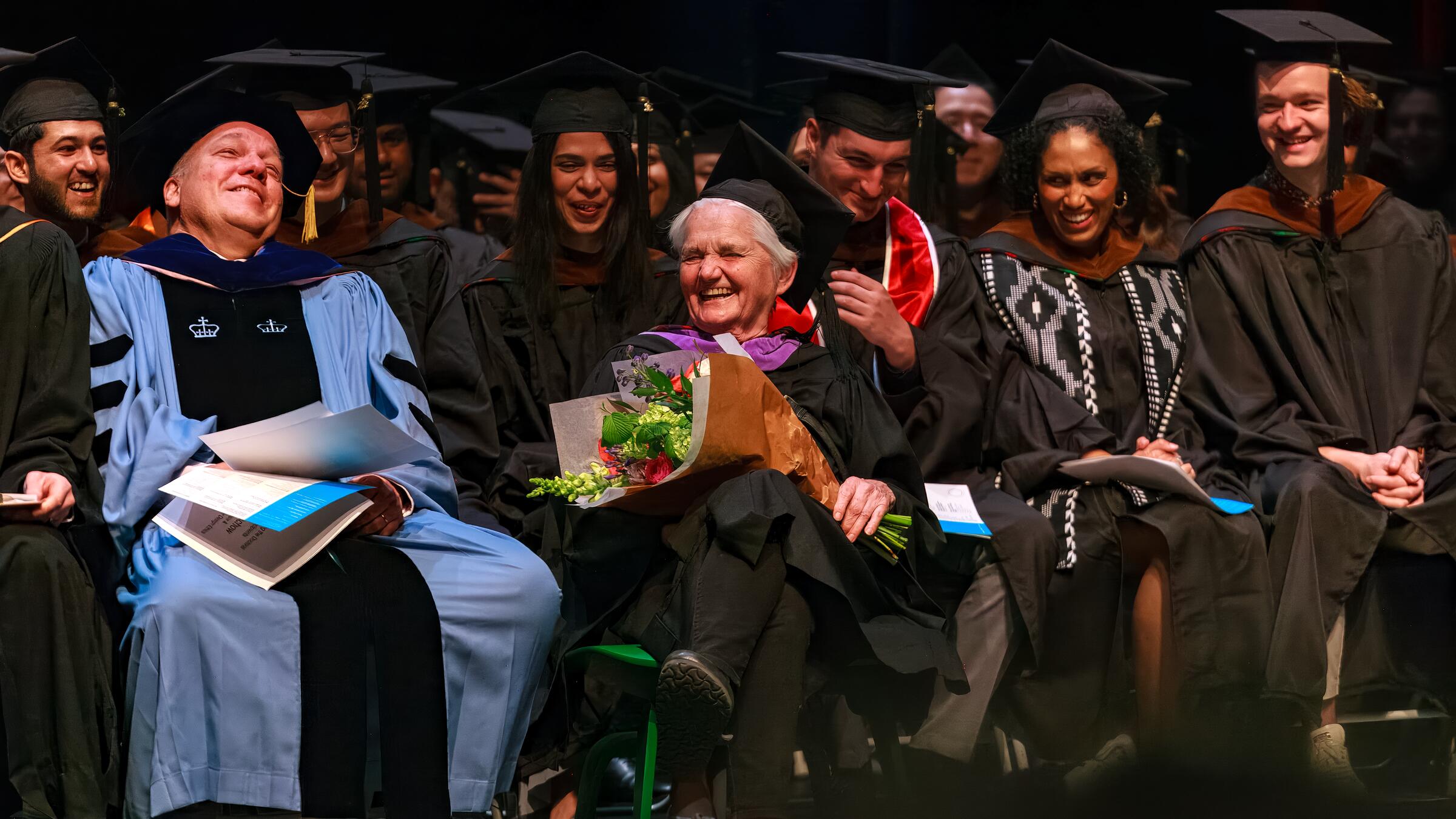 group sitting onstage in graduation regalia