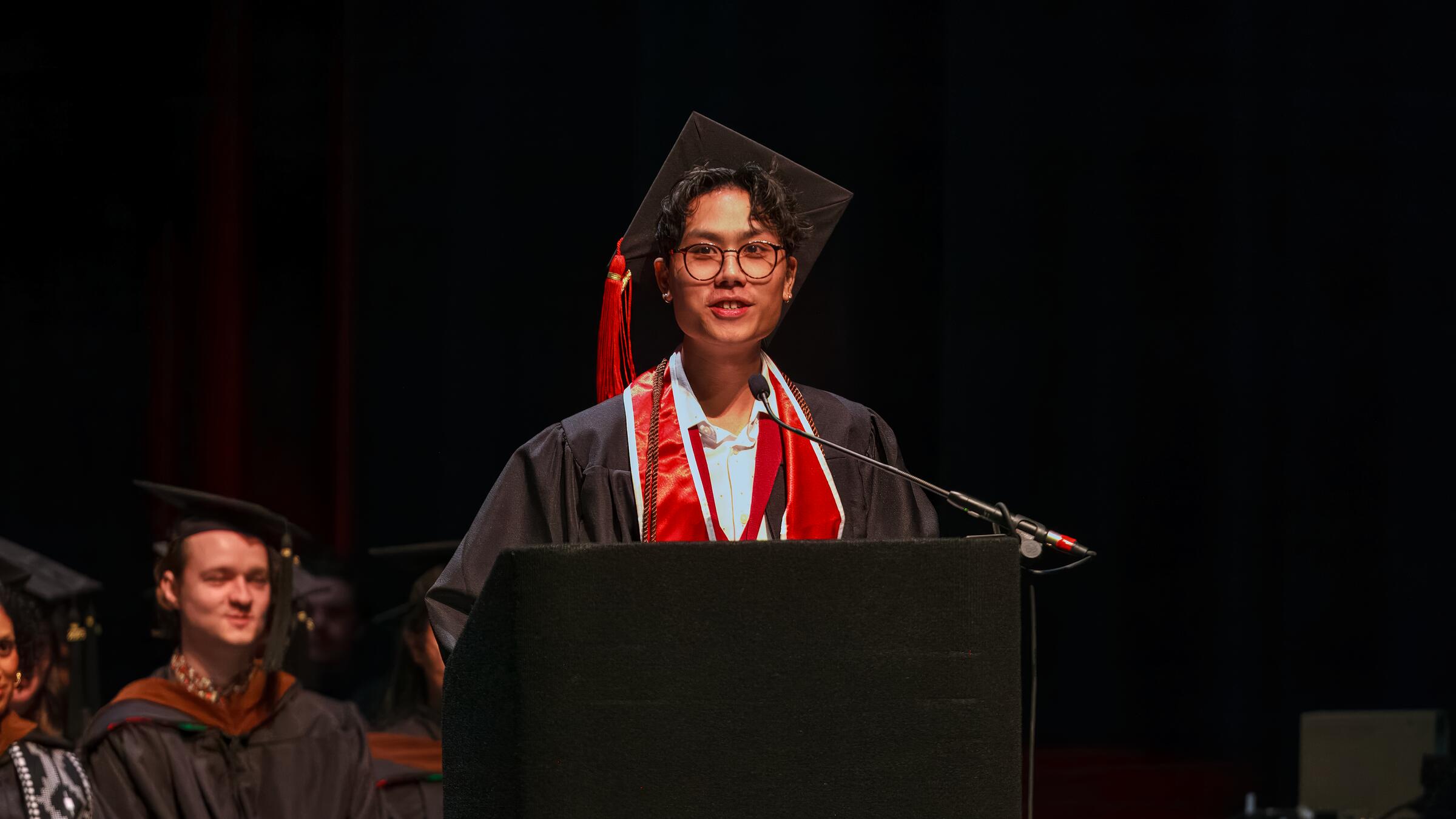 student onstage at podium in graduation regalia