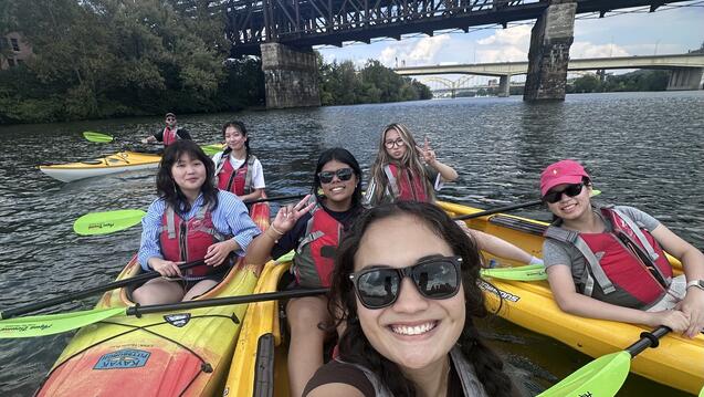 a group of students smiles for a photo in kayaks in a river