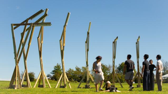 a group of people standing in a grassy field next to large wooden structures