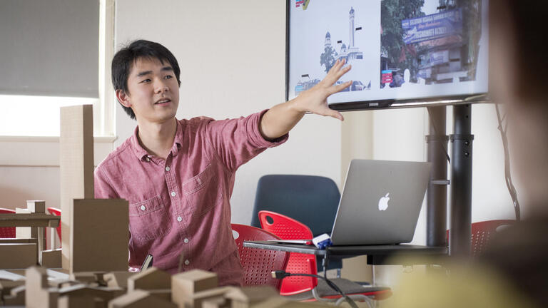 Student speaking in front of class in front of screen display