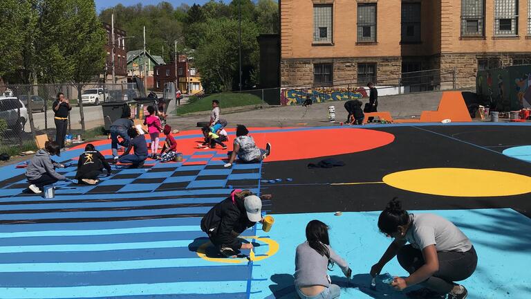 Photograph of children and community members painting a large mural on the ground
