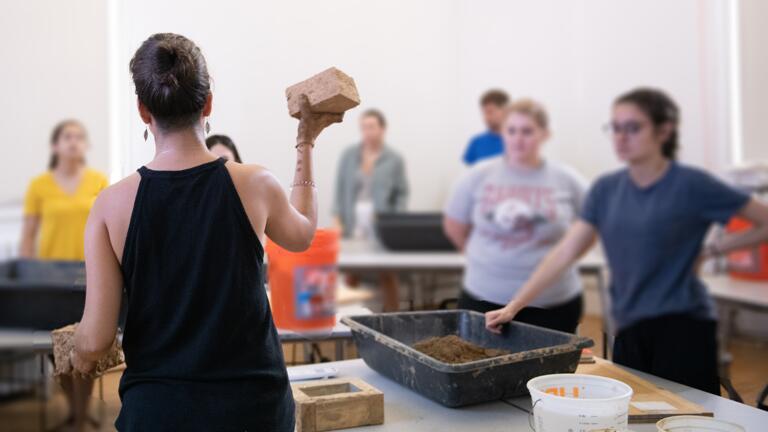 A teacher holds up a brick while speaking to a group of students