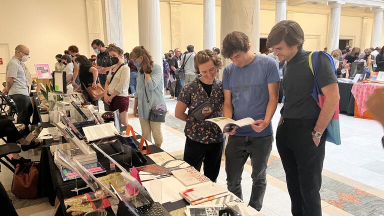 Visitors at the Carnegie Mellon Architecture table at the Pittsburgh Art Book Fair peruse a book.