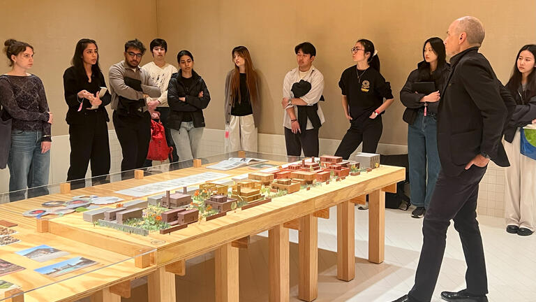 a group of students stands in a group around an exhibition on a large table