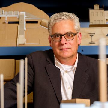 person with short hair and glasses surrounded by architectural models
