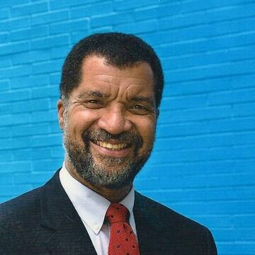 person wearing a suit in front of a bright blue brick wall