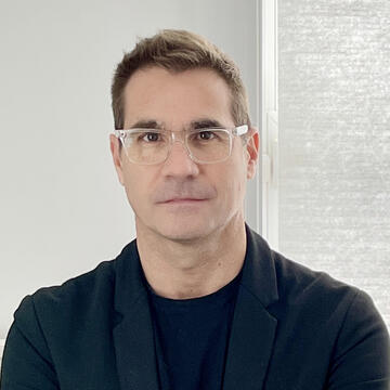 person with clear glasses wearing a dark blazer over a dark t-shirt Ruben Alcolea