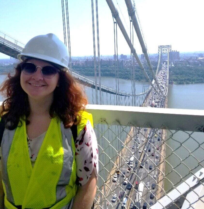 A woman wearing a hard hat and safety vest in front of a bridge