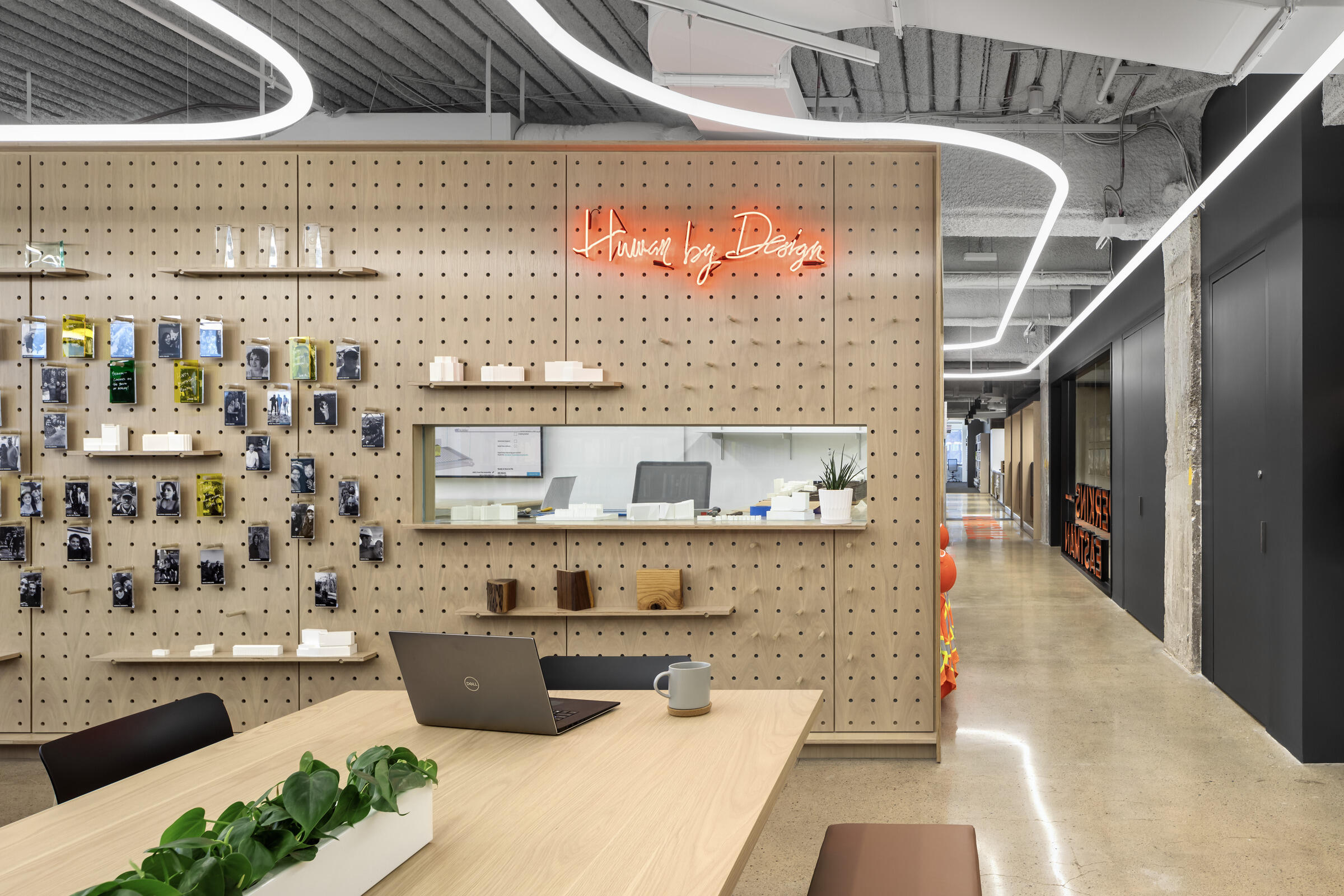 Interior of Perkins Eastman office in Pittsburgh with chipboard wall, wooden furniture and neon sign.